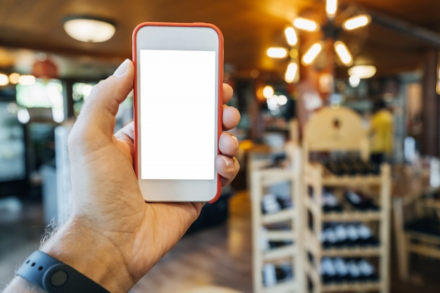 Foto telefon in der hand eines mannes in einem roten rahmen, in einem geschäft mit warmem licht und regalen mit lebensmitteln. konzept der produktauswahl in der online-bewerbung.