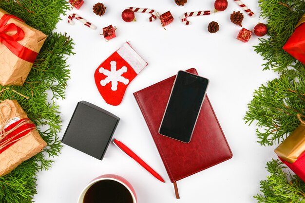 Telefon, Kaffeetasse auf Weihnachtsraum. Sicht von oben. Platz zum Schreiben. Leerraum. Gemütliche Ruhe. Latte Tasse, Notizbuch, Stift, Telefon, Geschenkverpackung. Nadeln.