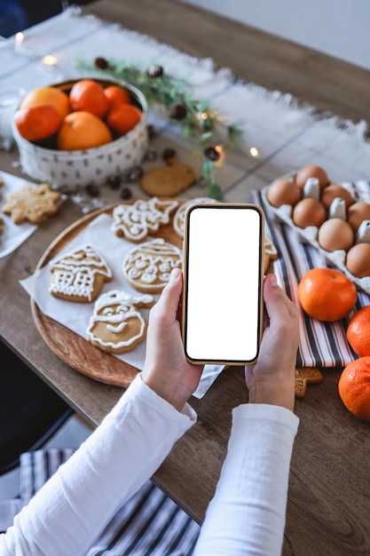 Telefon mit einem leeren Bildschirm in den Händen auf dem Hintergrund des Weihnachtskochens Platz für Text Meisterklasseneinladung Frohe Weihnachten