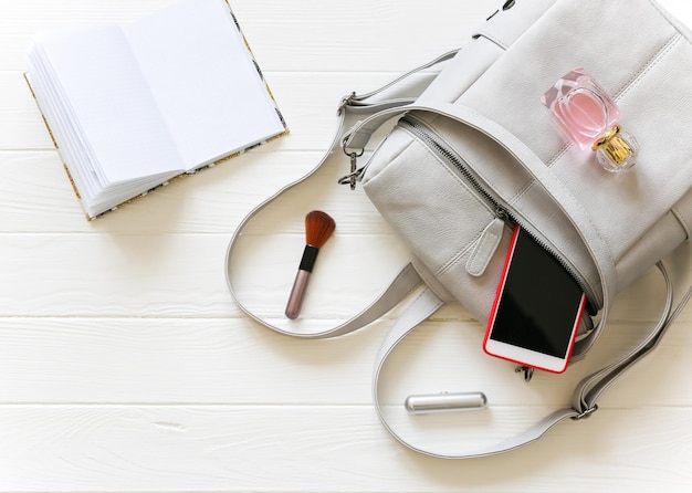 Telefon, stilvolle Tasche und Parfums auf weißem Hintergrund. Schöne flache Lage. Dinge für Geschäftsfrauen. Merken Sie sich den Stundenplan des Buches. Schminkkasten.