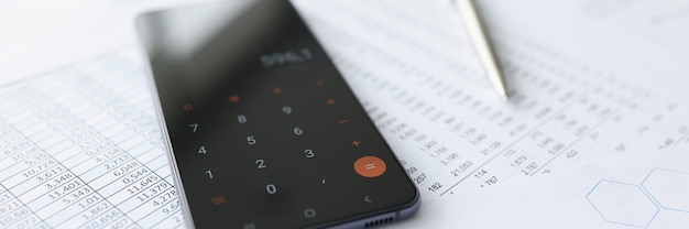Telefone celular com calculadora deitada em documentos close up calculando conceito de contas