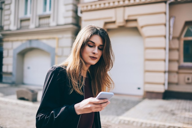 Telefone celular de mulher caucasiana na mão e mensagem de texto passeando ao ar livre no dia ensolarado do outono