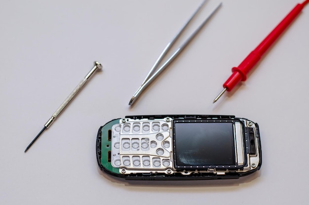 Telefone celular desmontado na mesa de um engenheiro mecânico durante o reparo Pinça e chave de fenda para reparar aparelhos eletrônicos em um fundo branco