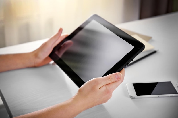 Telefone celular e mãos femininas usando tablet moderno dentro de casa