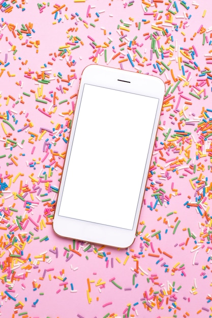 Telefone celular e polvilha doce colorido na tabela pastel cor-de-rosa no estilo liso da configuração.