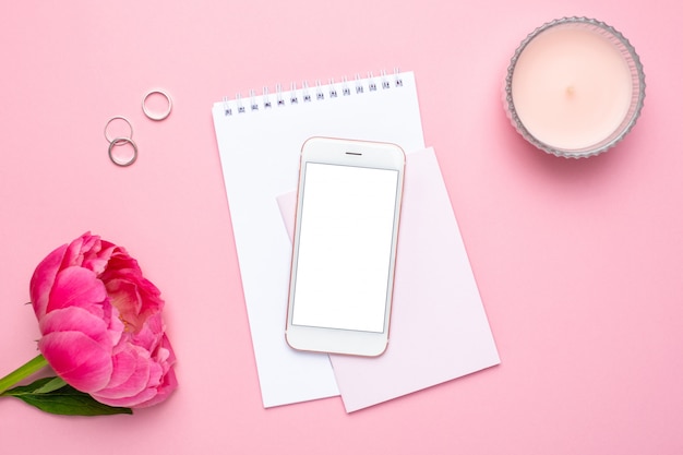 Telefone celular, notebook e peônia flor na mesa rosa pastel em estilo apartamento leigo.