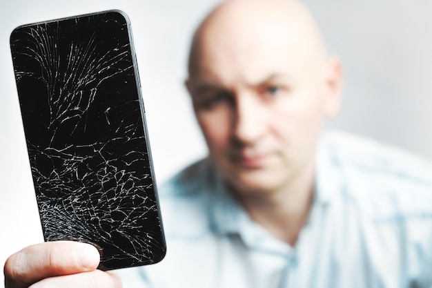 Telefone com tela quebrada Um homem branco está segurando um smartphone preto com uma tela rachada