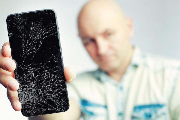 Telefone com tela quebrada Um homem branco está segurando um smartphone preto com uma tela rachada