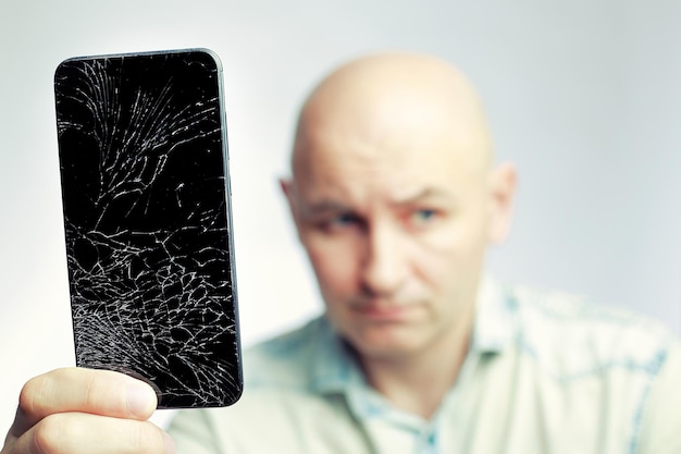 Telefone com tela quebrada Um homem branco está segurando um smartphone preto com uma tela rachada