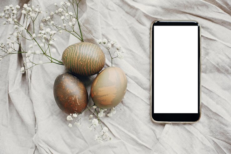 Foto telefone com tela vazia e elegantes ovos de páscoa deitados na mesa rústica com flores brancas de primavera ovos de páscoa tingidos naturais em têxteis rurais com smartphone espaço de maquete para texto