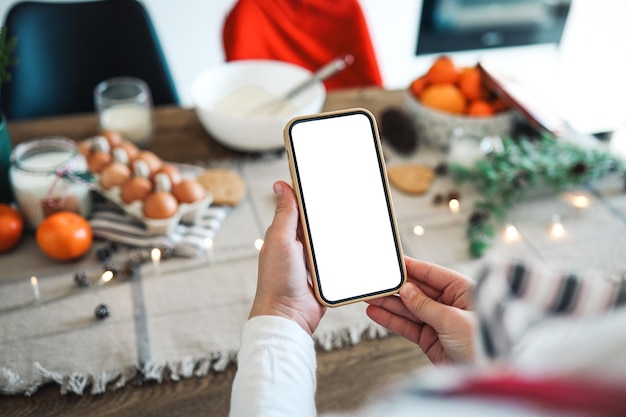 Telefone com uma tela em branco nas mãos no fundo da cozinha de Natal Lugar para texto Convite de classe mestre Feliz Natal