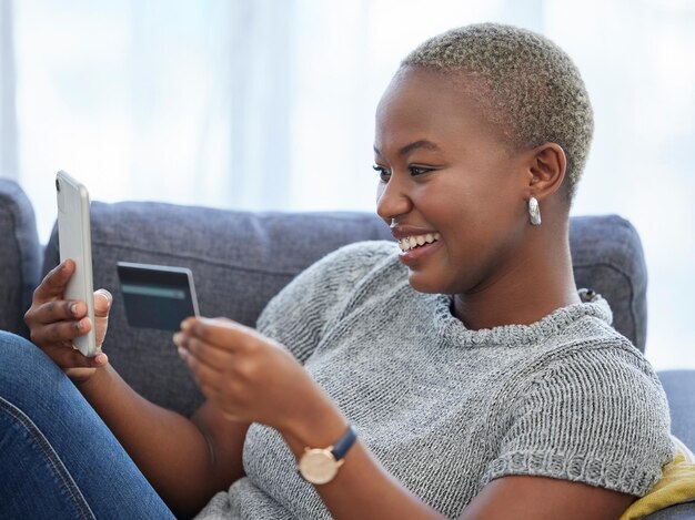 Telefone de comércio eletrônico e mulher negra feliz com um cartão de crédito fazendo compras on-line em um aplicativo de pagamento digital em casa Smile banking e uma garota africana animada verificam o crescimento do dinheiro do orçamento de caixa ou as economias on-line