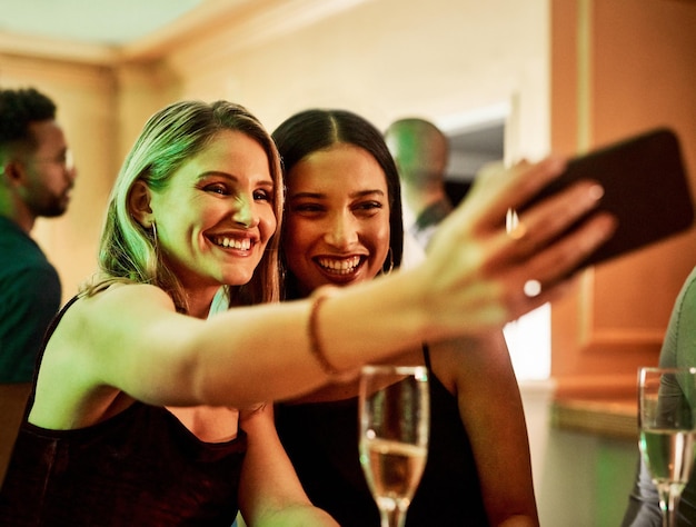 Telefone de festa ou amigos tirando uma selfie para conteúdo de mídia social ou para postar fotos de perfil felizes na noite das mulheres Meninas ou mulheres do evento tiram uma foto com bebidas de vinho ou champanhe para uma comemoração