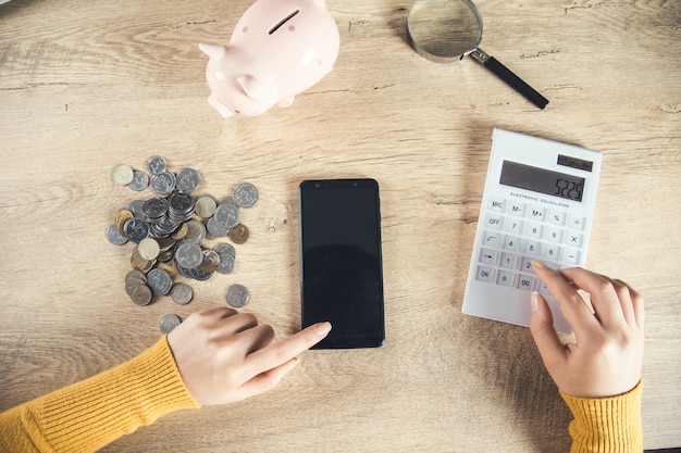 Telefone de mão de mulher com moedas e calculadora na mesa