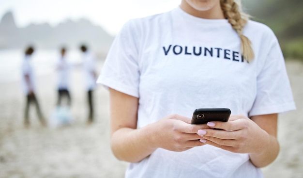 Telefone de mãos e mulher voluntária na praia para limpeza de mídia social e navegação na web Sustentabilidade ambiental do Dia da Terra e mulher com smartphone móvel 5g à beira-mar para serviço comunitário