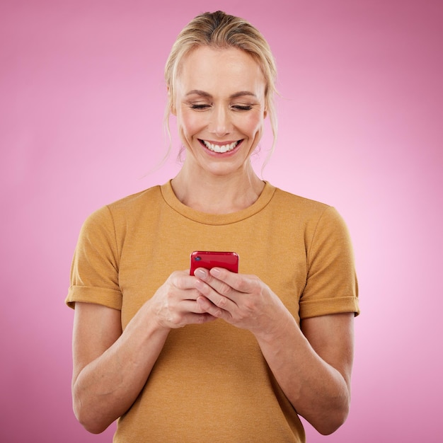 Telefone de mulher e fundo rosa para mídia social de comunicação e bate-papo online no estúdio Pessoa modelo feliz com smartphone nas mãos para conexão de rede ou postagem de digitação no aplicativo móvel ou site