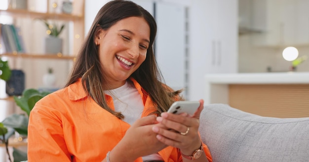 Telefone de mulher e rindo de meme de piada engraçada ou post de mídia social relaxando no sofá da sala em casa Mulher feliz conversando mensagens de texto e rindo no smartphone para se divertir comunicação on-line no sofá