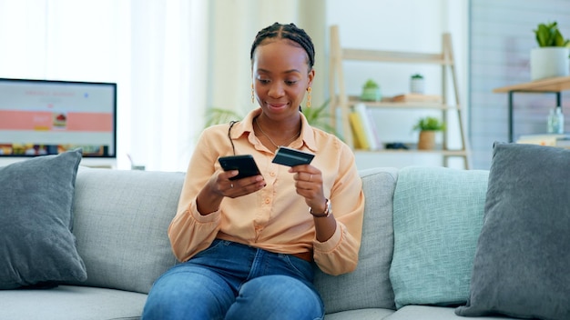 Telefone de mulher negra e cartão de crédito no sofá para pagamento de compras on-line ou fintech em casa Mulher africana feliz relaxando com débito ou smartphone móvel para aplicativo de banco de transação ou comércio eletrônico