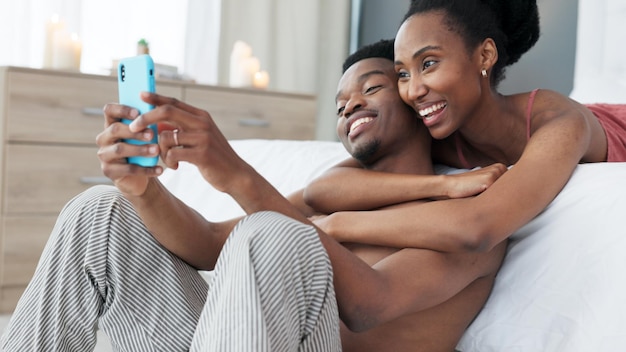 Telefone de retrato e casal tiram uma selfie no quarto juntos e compartilham no aplicativo de rede social online pela manhã Sorriso de mídia social e mulher negra adora tirar fotos com parceiro africano