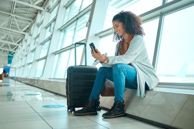 Foto telefone de viagem e mulher negra no aeroporto em uma videochamada esperando por viagens e voos de avião conexão móvel on-line e sorriso de uma jovem sentada no terminal de avião esperando transporte