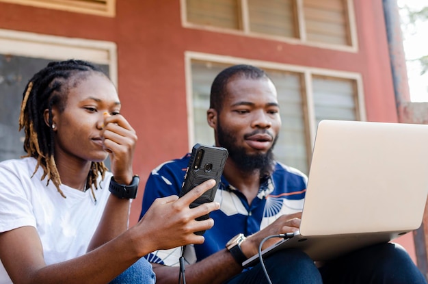 (telefone em foco) - imagem recortada de dois africanos compartilhando arquivo do laptop para o celular