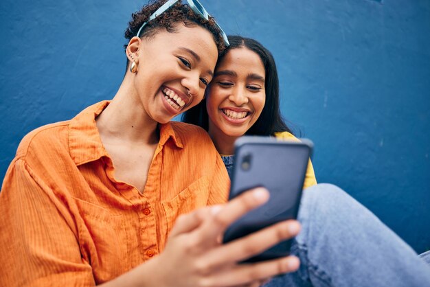 Foto telefone feliz e mulheres na cidade em fundo azul para postagem on-line de mídia social e navegação na internet sorriso de amizade e mulheres no smartphone na cidade urbana para férias e viagens de união