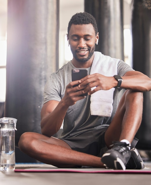 Telefone fitness e homem negro relaxam e sorriem para exercícios esportivos de comunicação on-line ou assistindo a um tutorial de exercícios na academia Vídeo de bem-estar de treinamento de felicidade no celular e descanso após corrida cardio