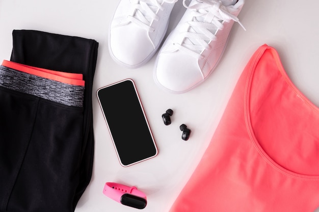 Foto telefone, fones de ouvido, relógio com roupas esportivas e tênis em fundo branco