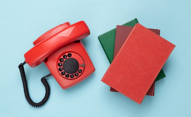 Telefone giratório antiquado vermelho retrô e livros sobre fundo azul Vista superior