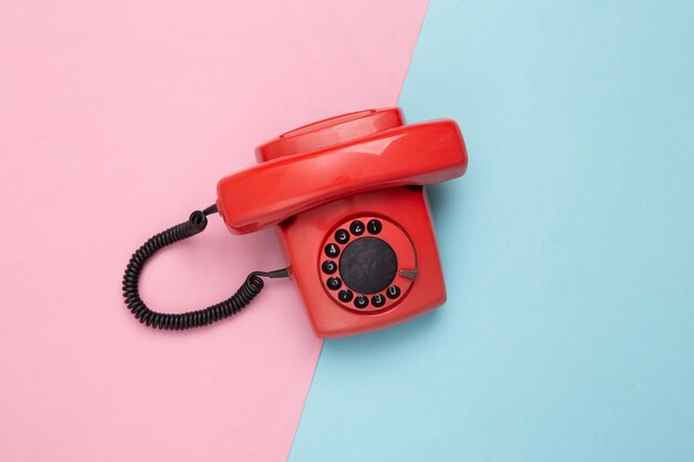 Telefone giratório antiquado vermelho retrô sobre fundo azul rosa vista superior