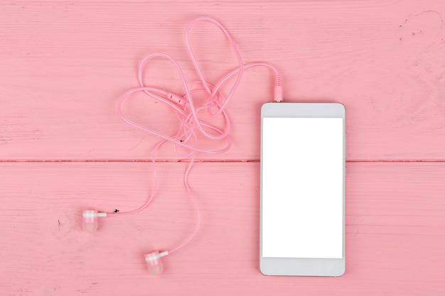Telefone inteligente branco com tela de toque em branco e fones de ouvido rosa na mesa de madeira rosa