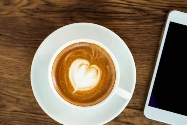 Telefone inteligente com café de latte art em fundo de madeira