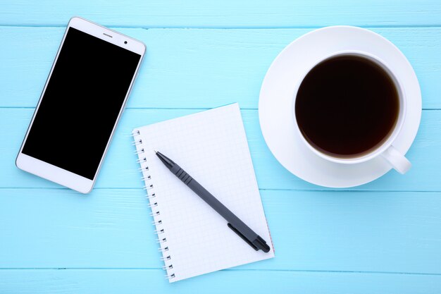 Telefone inteligente com notebook e xícara de café em madeira azul