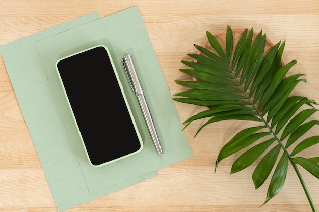 Telefone inteligente verde em branco na mesa de escritório de madeira Papel reciclado Caneta de papel comercial e telefone celular Mock Up