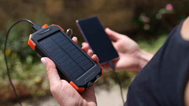 Telefone móvel e banco de energia solar em closeup de mãos