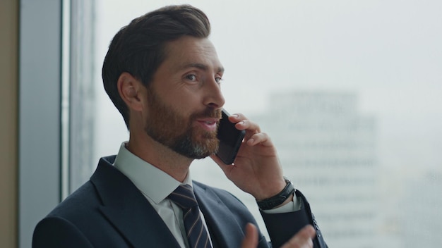 Telefone móvel falando do empresário perto da janela do escritório fechando a conversa de negócios