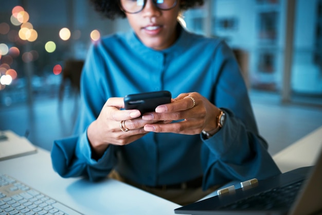 Telefone noturno e mãos de mulher de negócios no escritório com texto de mídia social ou comunicação por bate-papo mensagem de trabalho até tarde e empreendedora com aplicativo de smartphone para pesquisa ou leitura na internet