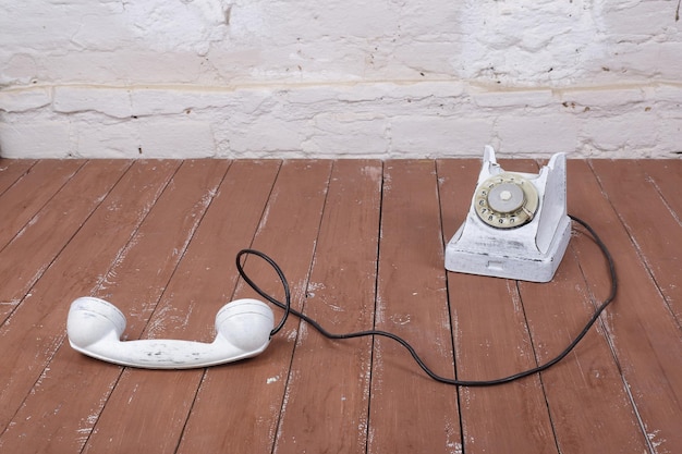 Telefone vintage branco com a captação em um fundo de madeira e parede branca