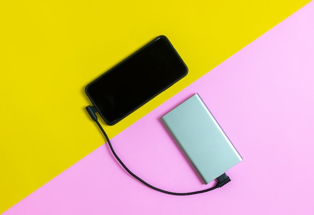 Telefones móveis de Smartphone que cobram baterias pelo fundo cor-de-rosa e amarelo do banco do poder