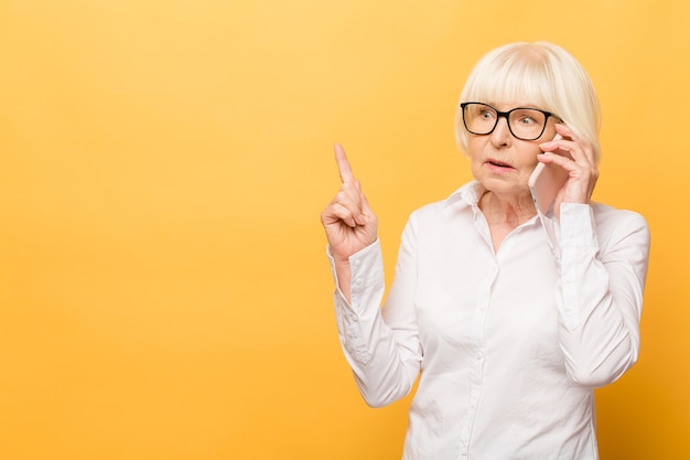 Telefongespräch. Gealterte Frau beim Sprechen am Telefon lokalisiert über gelbem Hintergrund.