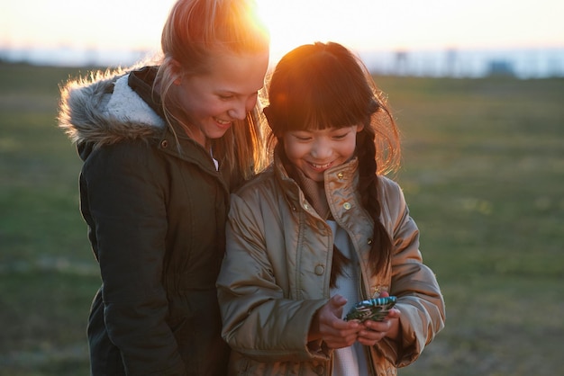 Telefonieren Sie Kinder und Freunde im Park auf Social Media Internet-Browsing oder Web-Scrolling Technologie-Smartphone und glückliche Kinder oder Mädchen mit Handy zum SMS-Streaming oder Spielen im Freien bei Sonnenuntergang