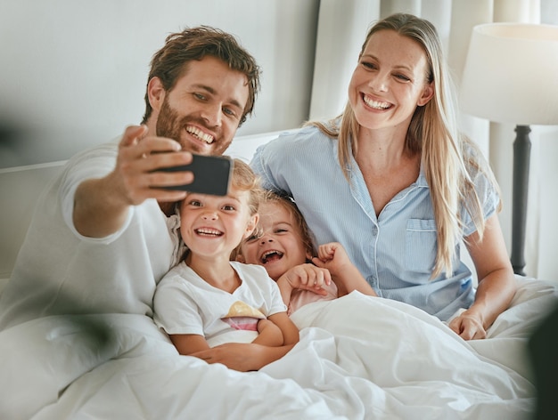 Telefonieren Sie mit der Selfie-Familie und entspannen Sie sich im Bett. Lächelnd für mobile Fotos für soziale Medien. Glückliche Eltern freuen sich über lächelnde Kinder und digitales Tech-Smartphone im Schlafzimmer zu Hause