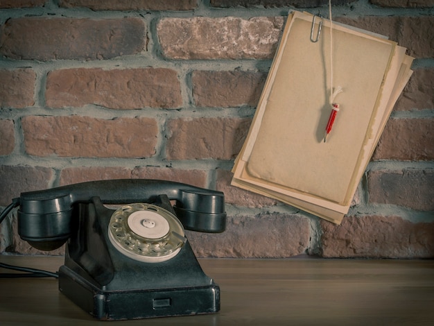 Teléfono antiguo y papel con un lápiz sobre una pared de ladrillos