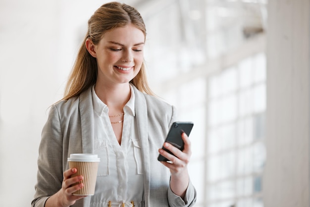 Teléfono café y en línea de un joven empleado enviando mensajes de texto en un teléfono inteligente en una oficina corporativa Sonrisa feliz y mujer móvil en Internet en el trabajo Redes de noticias y redes sociales en la oficina