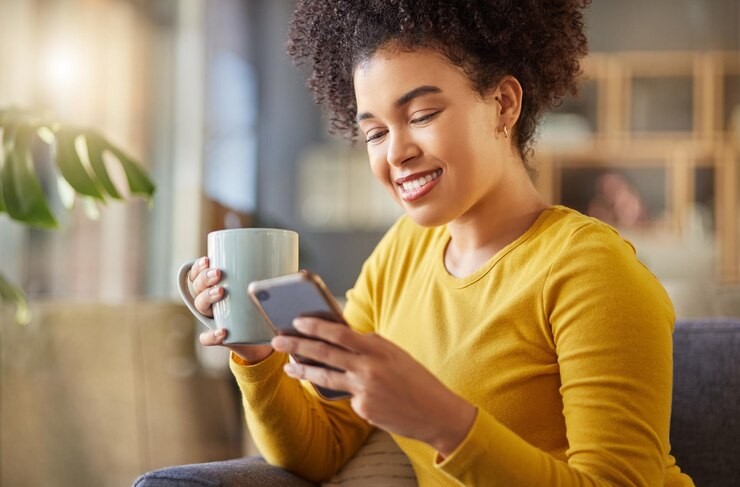 Foto teléfono café y mujer feliz en el sofá con inspiración en las redes sociales de internet y búsqueda de ideas para el hogar beba té y relaje a una persona joven o africana en una aplicación móvil para comunicarse o chatear en el sofá