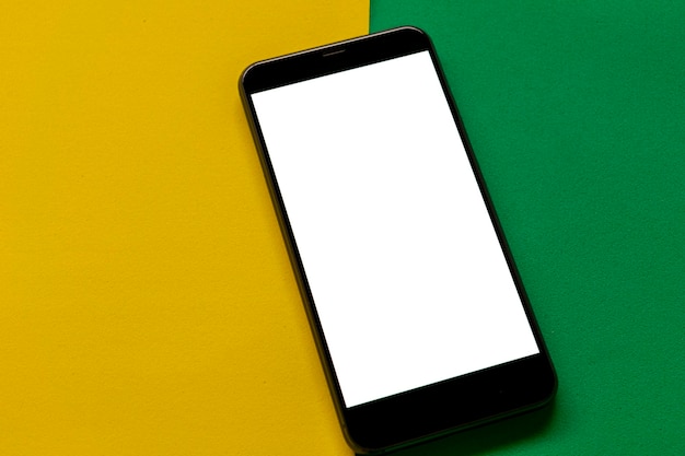 teléfono celular con pantalla en blanco sobre fondo verde y amarillo