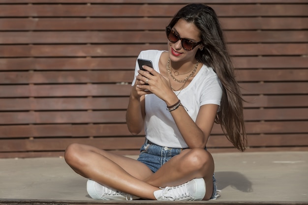 Teléfono celular de surf femenino positivo mientras se relaja en el escenario