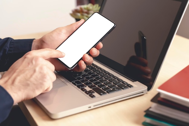 Teléfono y computadora portátil en la mano en el escritorio en la oficina o en casa maqueta de pantalla en blanco de teléfono inteligente