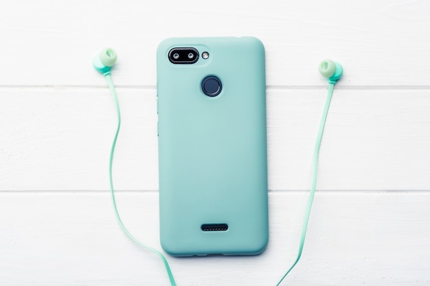 Foto teléfono digital azul con protección corporal y auriculares azules en la mesa blanca