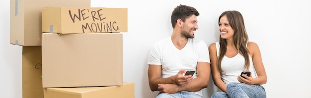 El teléfono de la feliz pareja cerca de las cajas en el fondo de la pared blanca